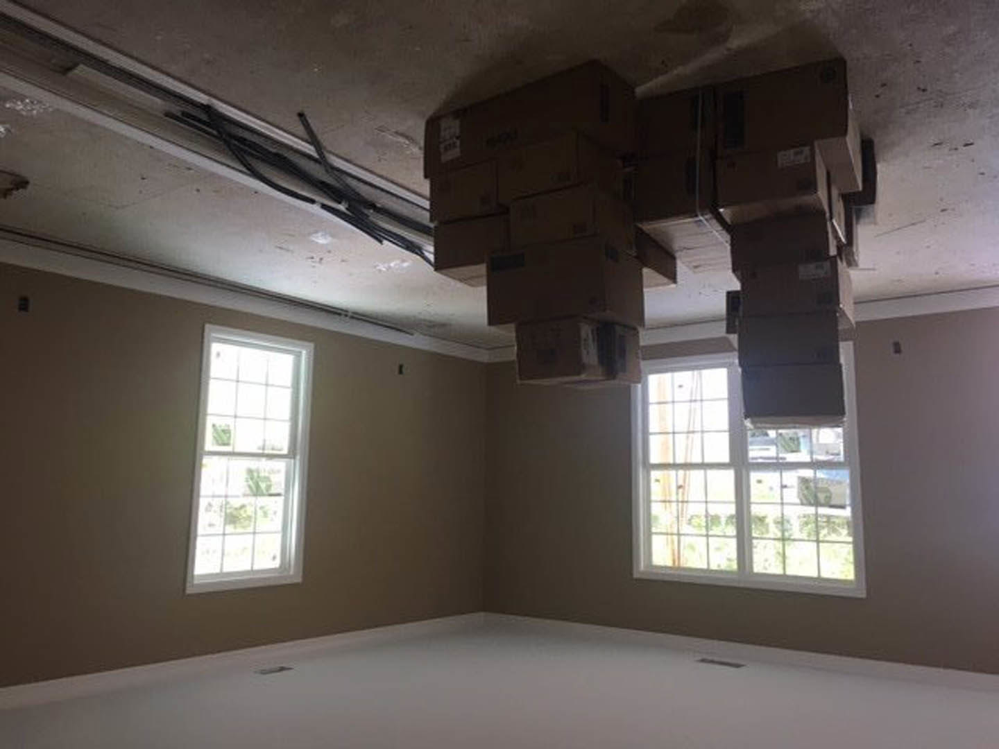 White plaster ceiling with stacked wooden box beams, multi-pane window with roller shade, black pipe fixture, and light-filled modern interior.