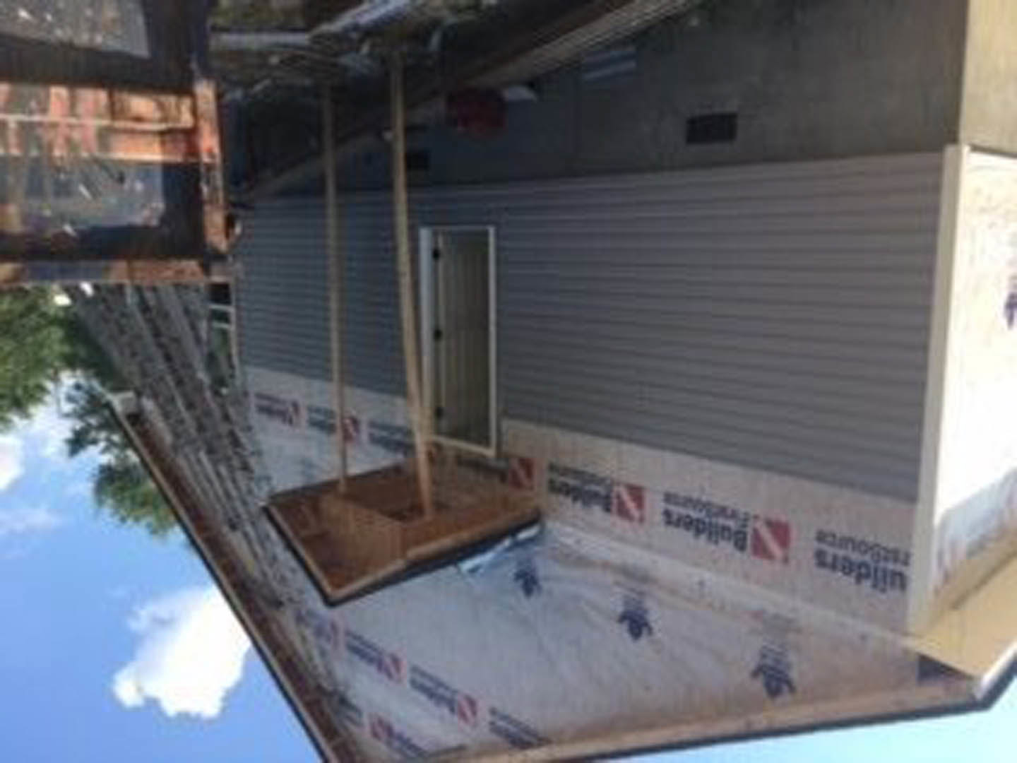 Partially constructed home exterior featuring a metal garage door, exposed framing, and unfinished walls under a clear sky