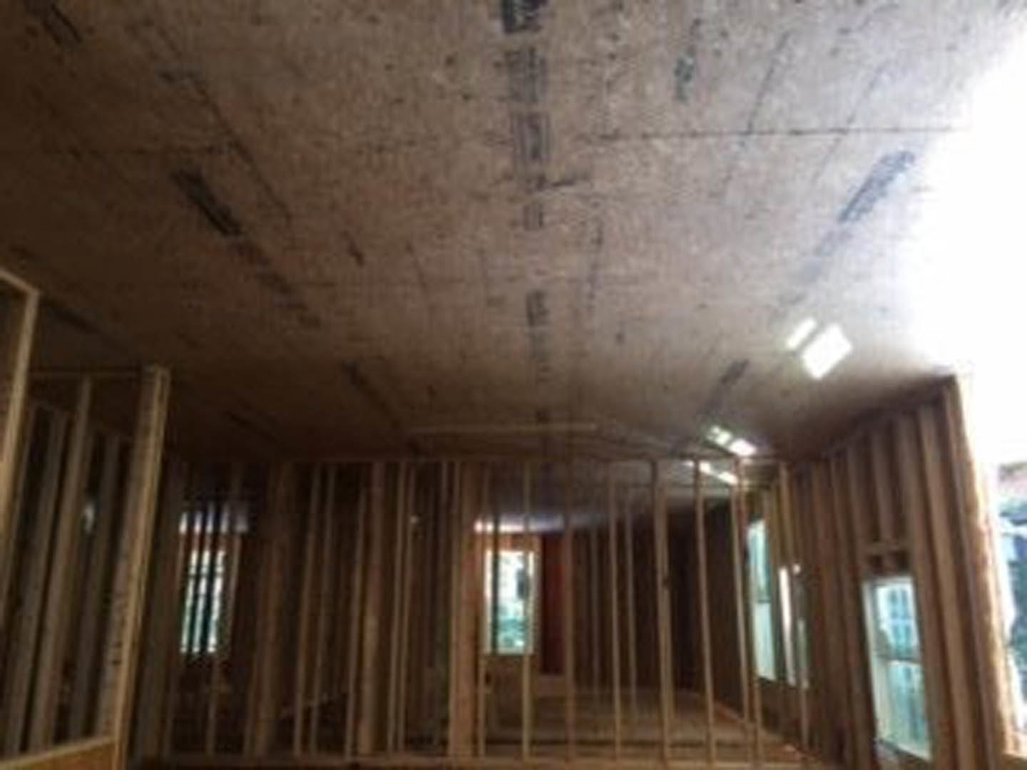 Unfinished room with exposed wood framing, ceiling marked with black construction text, partially visible window, and blurred figure in foreground