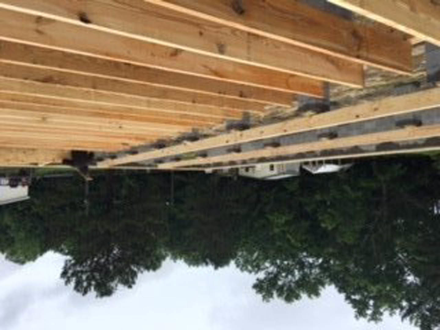 Stacked wooden planks on an outdoor construction site with a partially built structure and distant trees visible