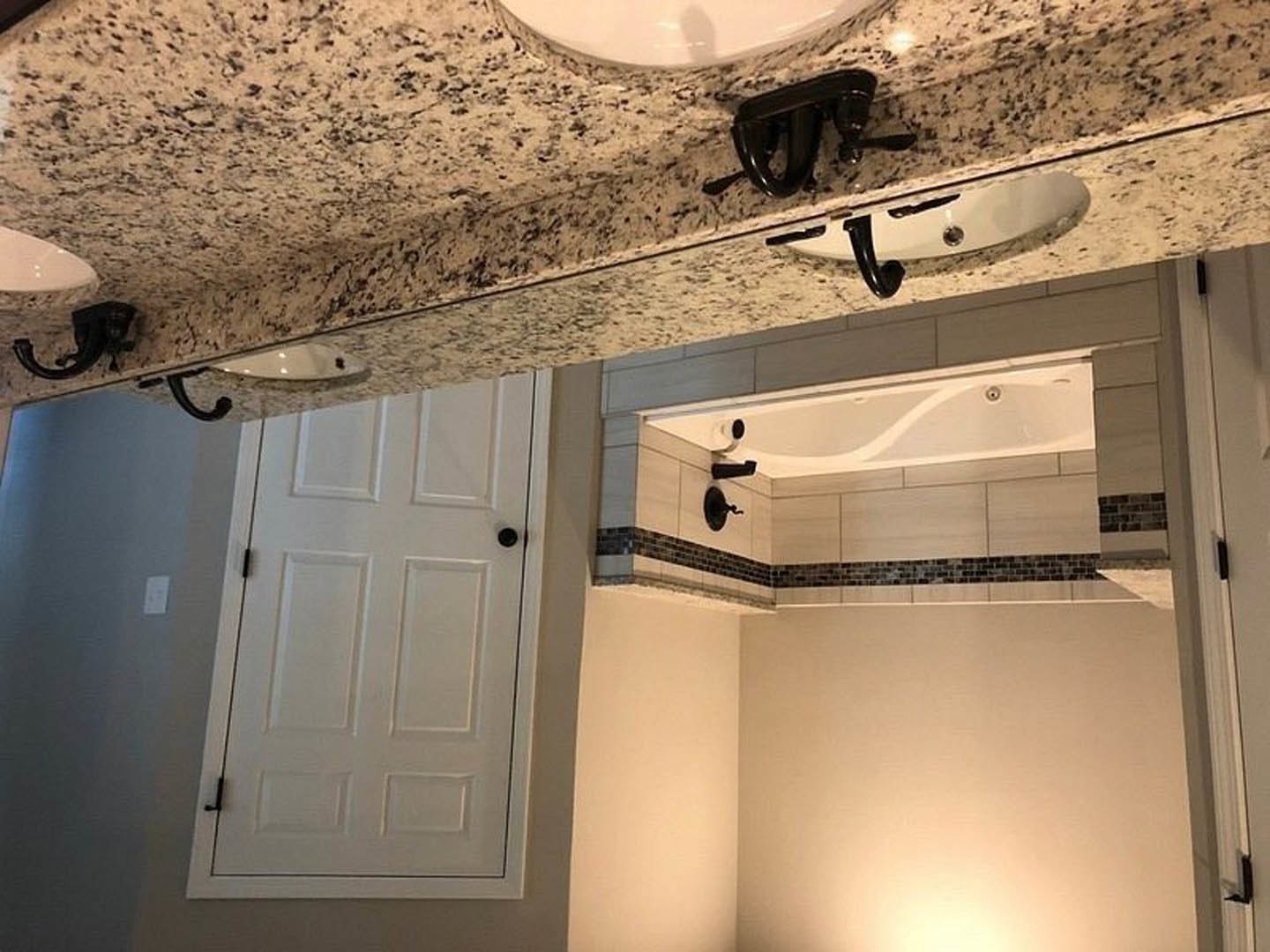 Marble countertop with white sink and black faucet, white cabinetry with black handles, curved white ceiling, blurred shadow reflected on wall