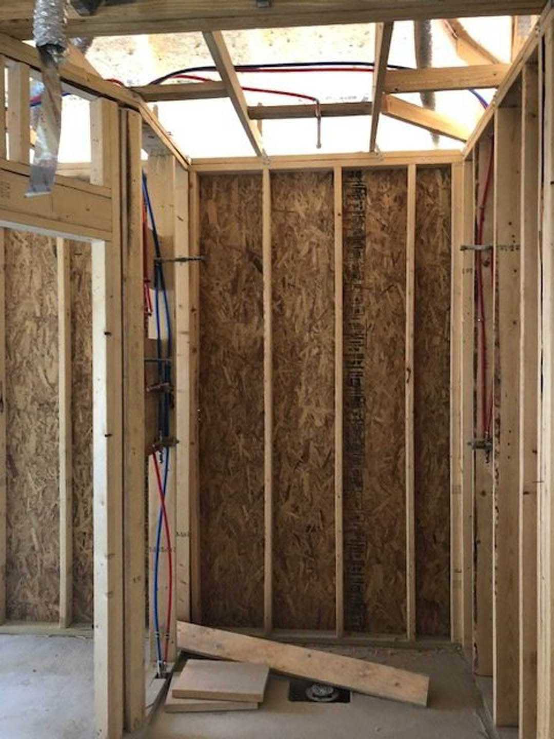 Exposed wood framing and beams with unfinished walls, visible ceiling wires, and construction materials scattered on the floor