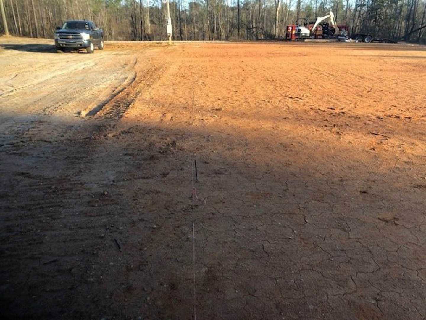 Dirt road leading to a parked truck, surrounded by trees and open soil under a clear sky