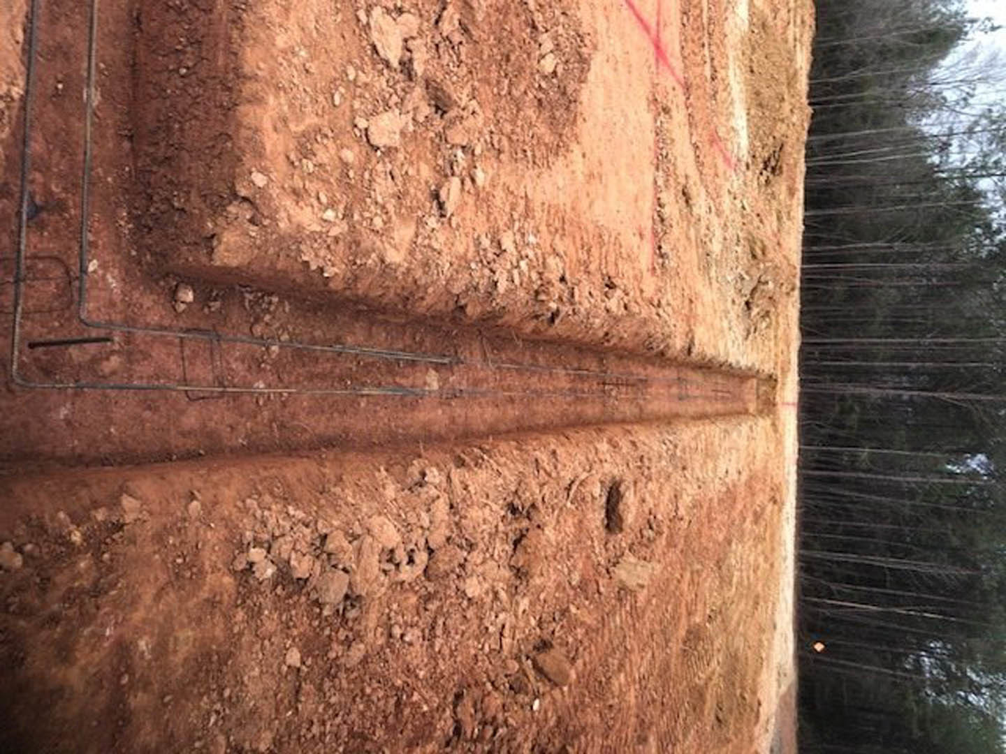 Dirt road lined with metal rods, surrounded by brown earth and scattered rocks, outdoor setting with trees in the background