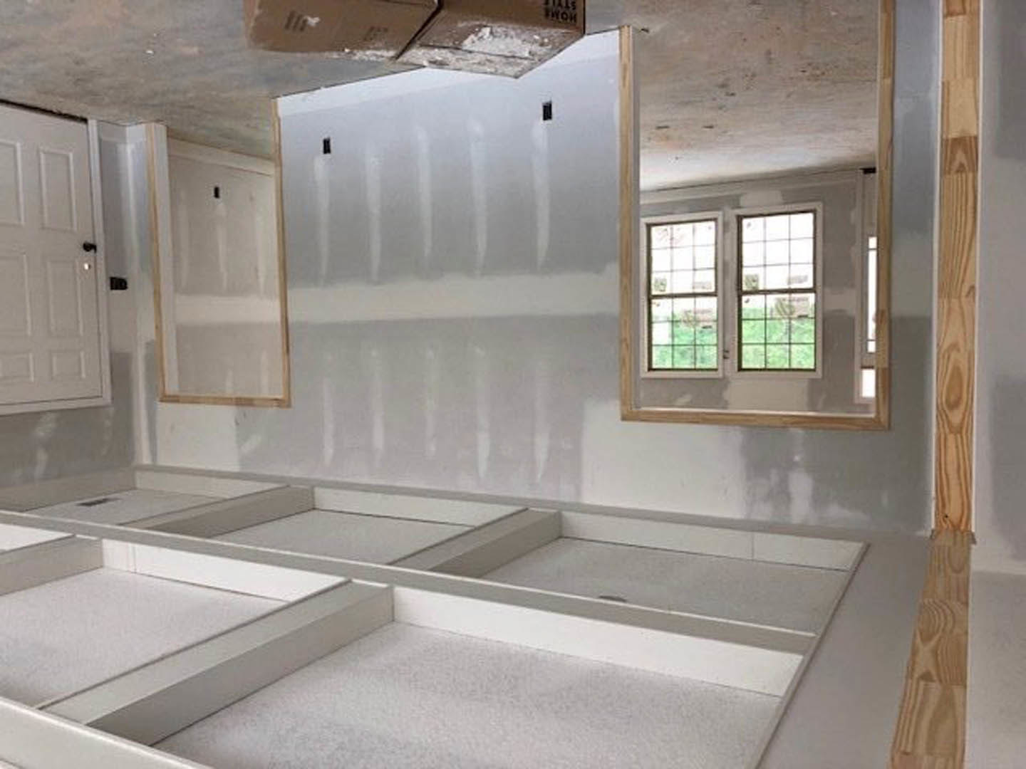 Bathroom with white plaster walls and ceiling, white tile floor, white framed window, white door with black handle, built-in white shelf, sink and shower fixtures, countertop