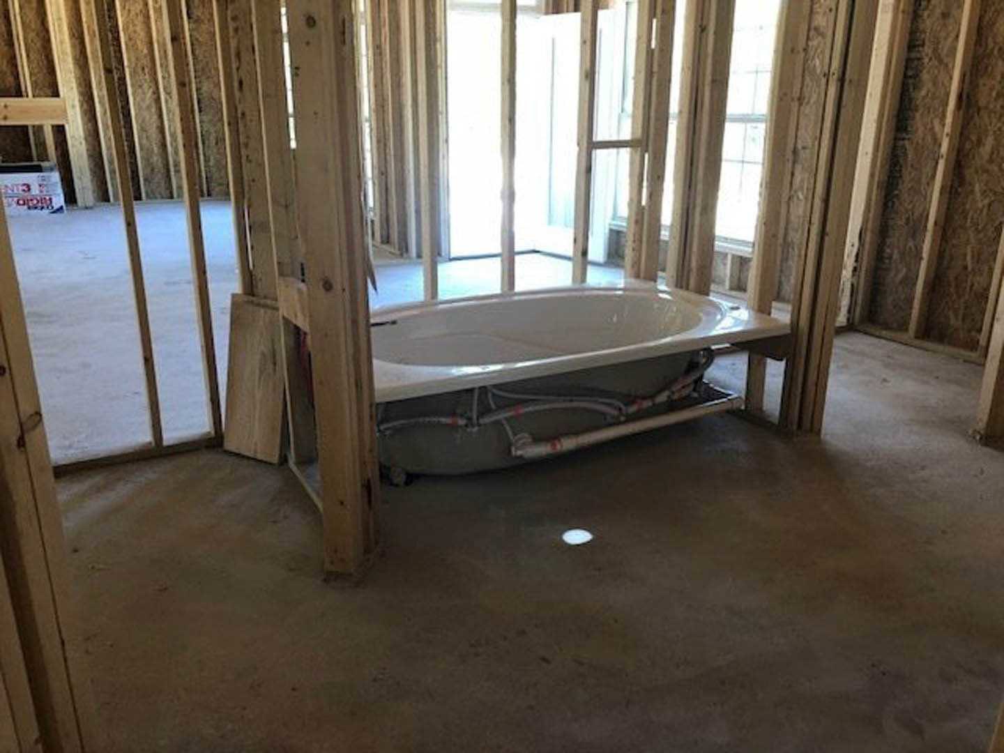 White freestanding bathtub partially installed in a room with unfinished flooring, exposed walls, and construction materials nearby