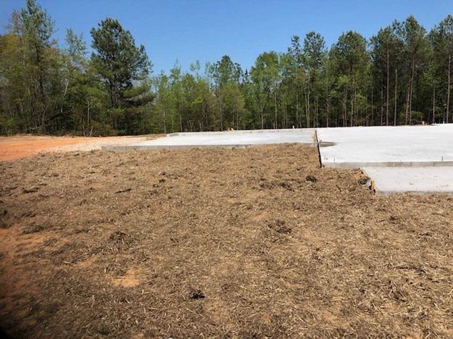 Concrete foundation slab set in grassy field with mature trees and blue sky in background