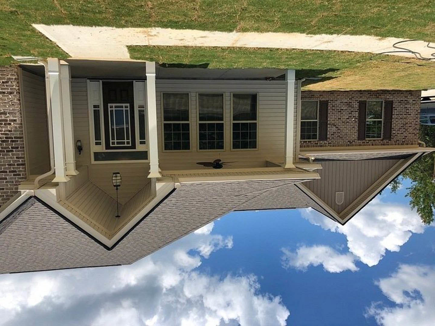 Two-story house with gray siding, white trim, large windows, gabled roof, manicured green lawn, and blue sky with scattered clouds