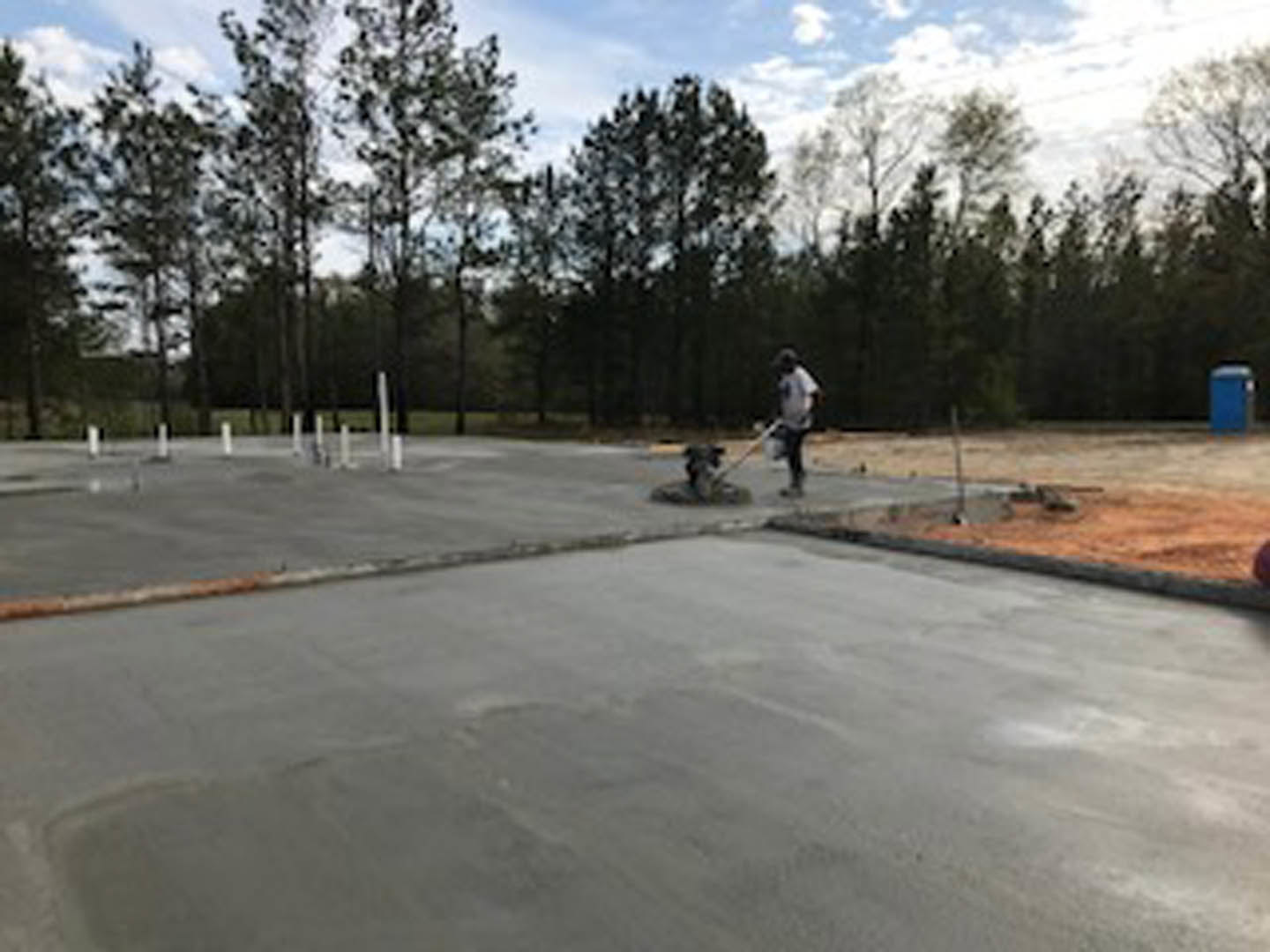 Modern two-story home with white stucco exterior, large windows, and dark wood accents; landscaped front yard with young trees and concrete driveway; man in white shirt standing