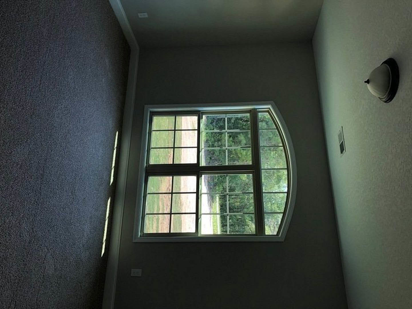 Bright room with large green-framed window overlooking grassy field, white walls, ceiling light fixture, and blue fabric accent