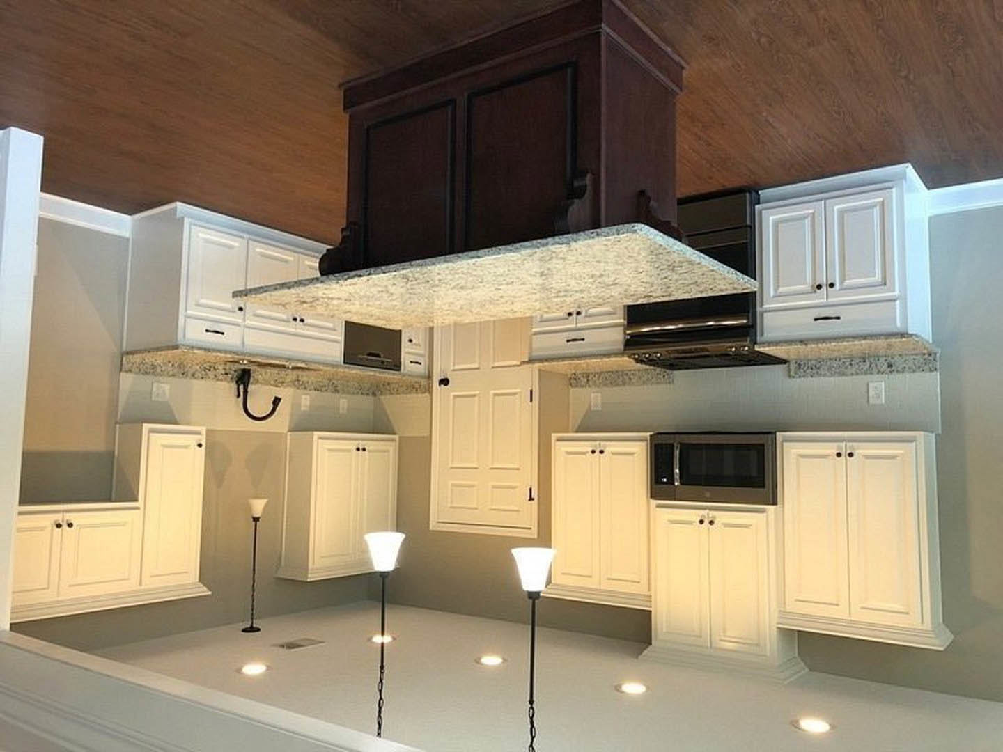 White kitchen cabinets, stainless steel stove with range hood, light-colored countertops, built-in microwave, recessed ceiling light, black support pole, smooth white surfaces