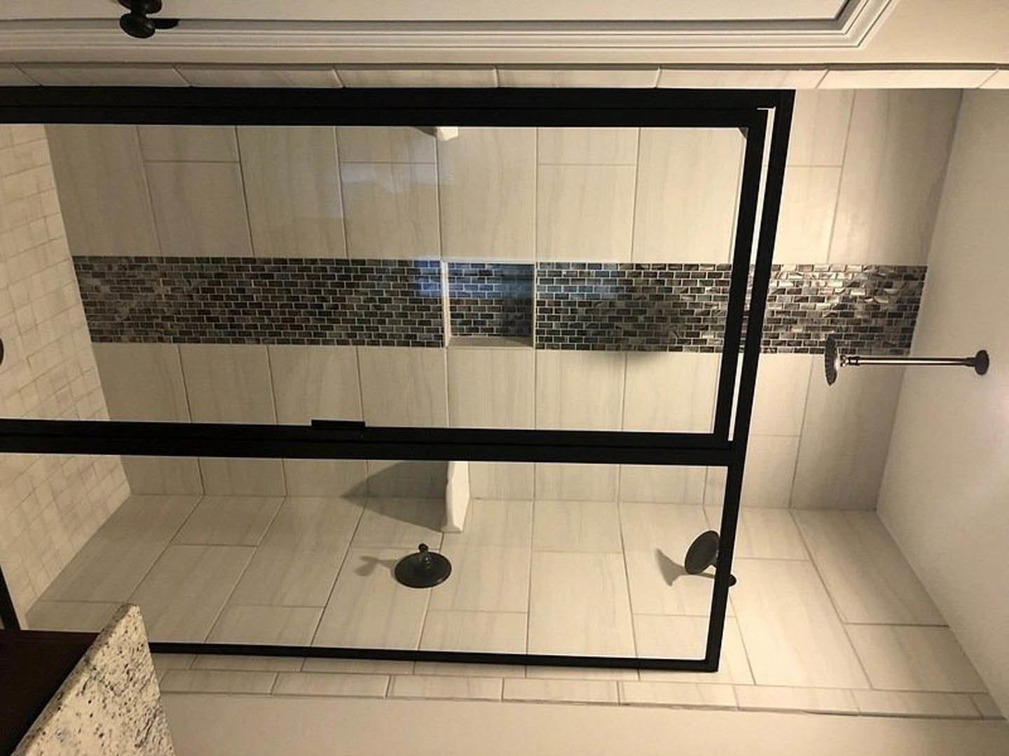 Shower with black-framed glass doors, white tiled floor, close-up of countertop, black round object on tile, white wall, bathroom interior