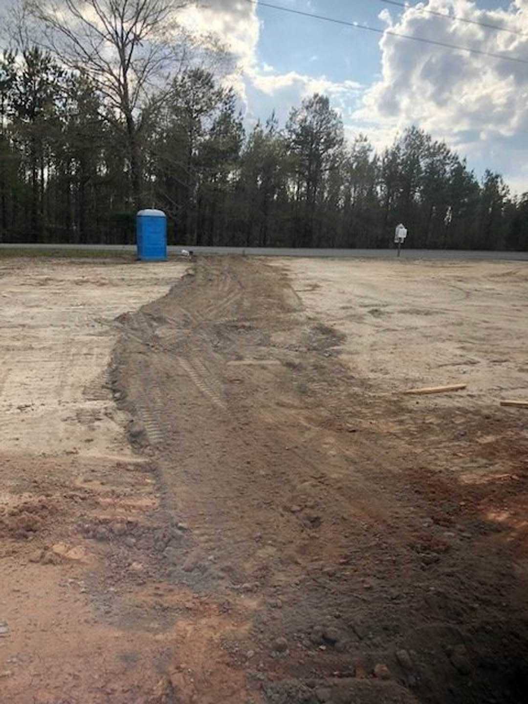 Dirt road bordered by trees under a cloudy sky, blue trash can with white lid positioned in the center