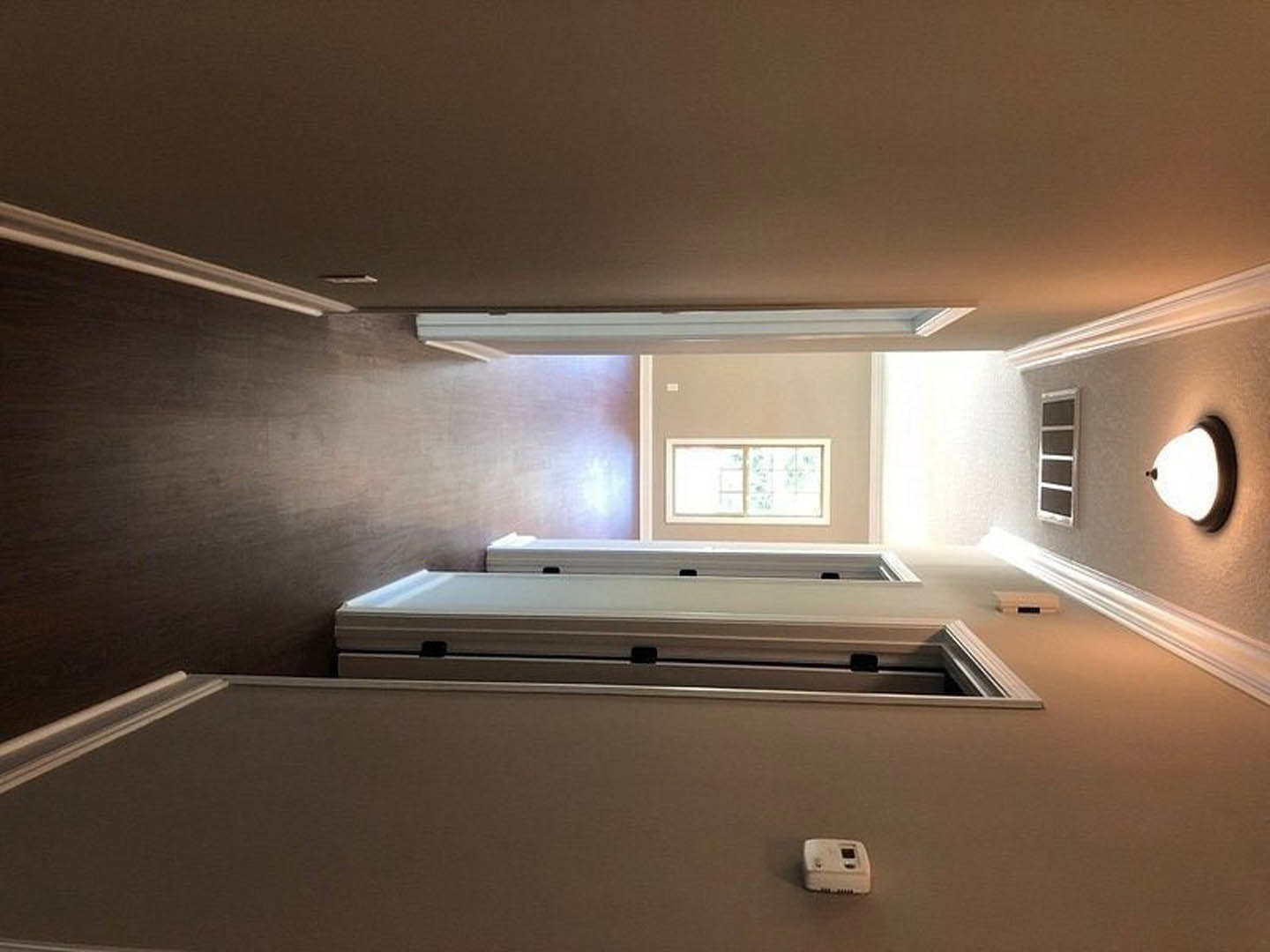 Hallway with white plaster walls, multiple doors, and a window with a white frame; ceiling light fixture visible