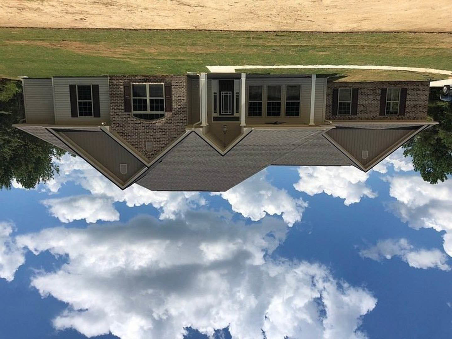 Modern house exterior with large windows reflecting nearby tree and green lawn, white framed windows, rectangular glass door, under blue sky with scattered clouds
