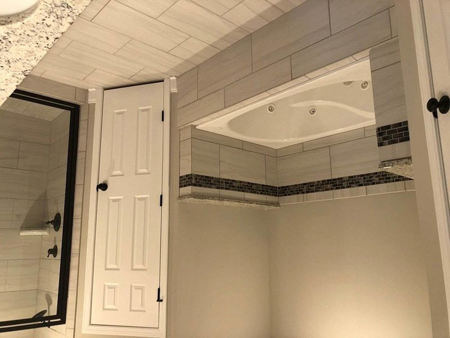 Bathroom with white paneled door featuring a black handle, freestanding white tub, light tile flooring, and wall-mounted mirror.