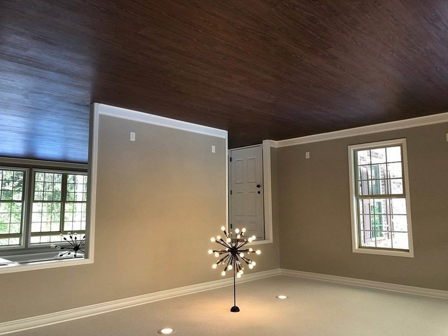 Chandelier with multiple lights hanging from a white ceiling, large multi-pane windows with daylight streaming in, white door with black hardware, decorative wall molding, plaster
