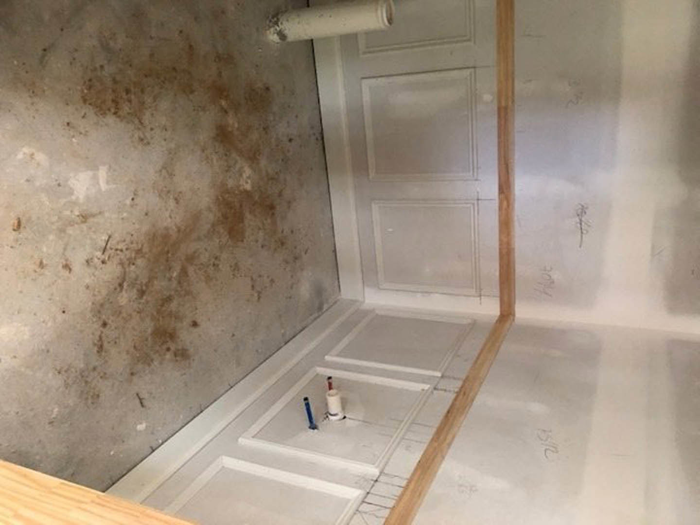 White paneled door with blue and red screws, adjacent to a plaster wall marked with black spots and dirt, marble floor showing visible grime.