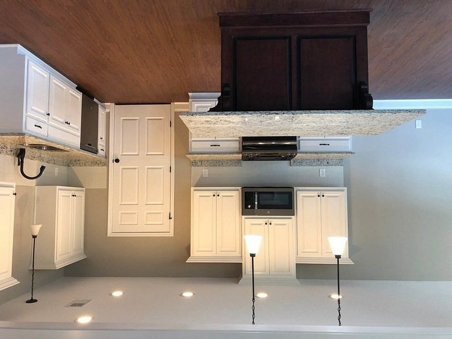 White kitchen cabinets with stainless steel microwave above a light-colored countertop, neutral backsplash, and upper cupboards