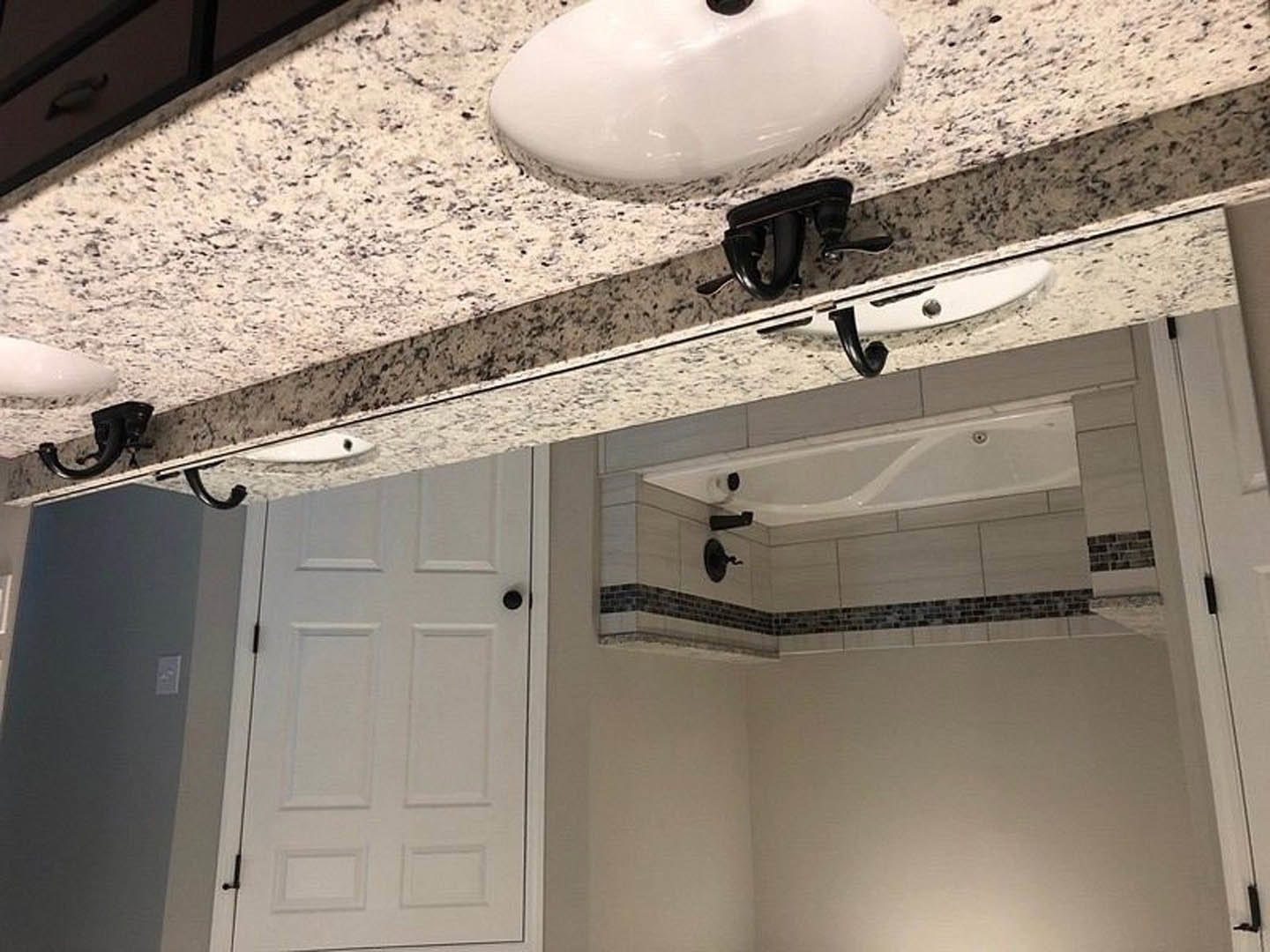 Marble countertop with black faucet, white sink, white door with black knob, and bathtub in a modern bathroom