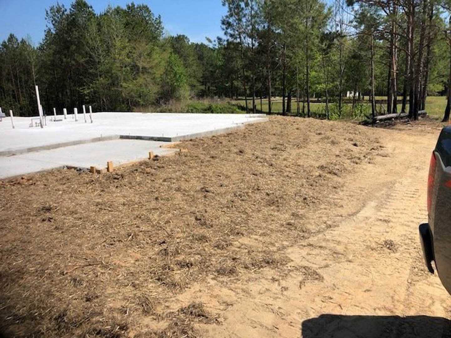 Concrete slab bordered by a dirt path, surrounded by grass and trees under an open sky