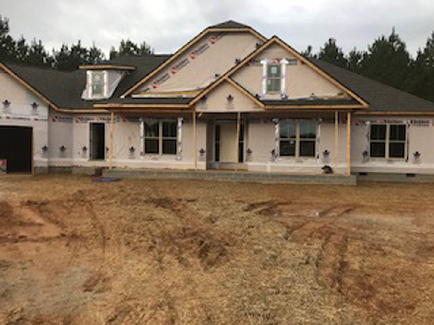 Two-story house with gray siding, white trim, gabled roof, large windows, and manicured green lawn in front yard under partly cloudy sky
