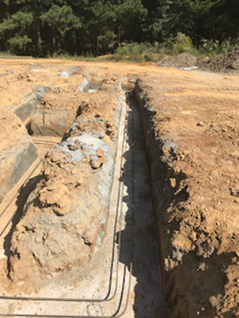 Excavated dirt trench with exposed soil and rocks, surrounded by trees and plants in a forested outdoor setting