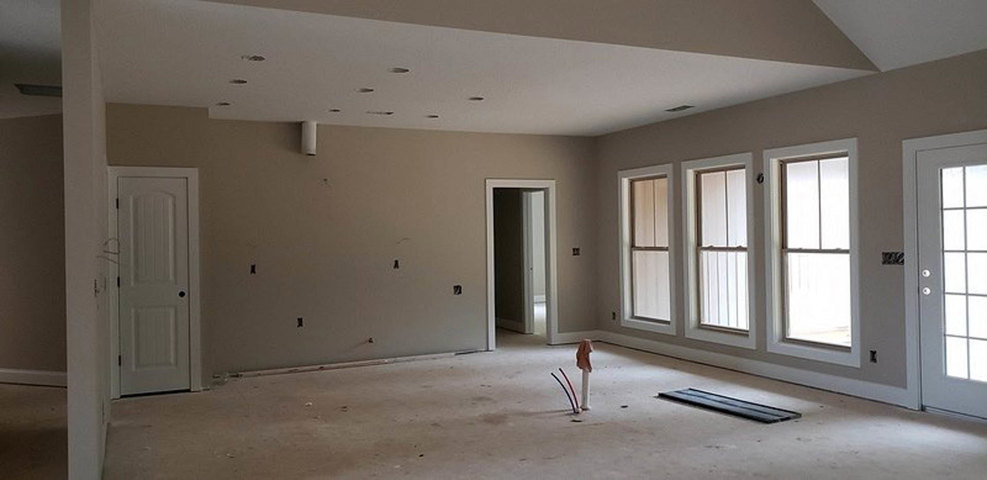 Bright room with light-colored plaster walls, several rectangular windows, white swinging door, and smooth flooring