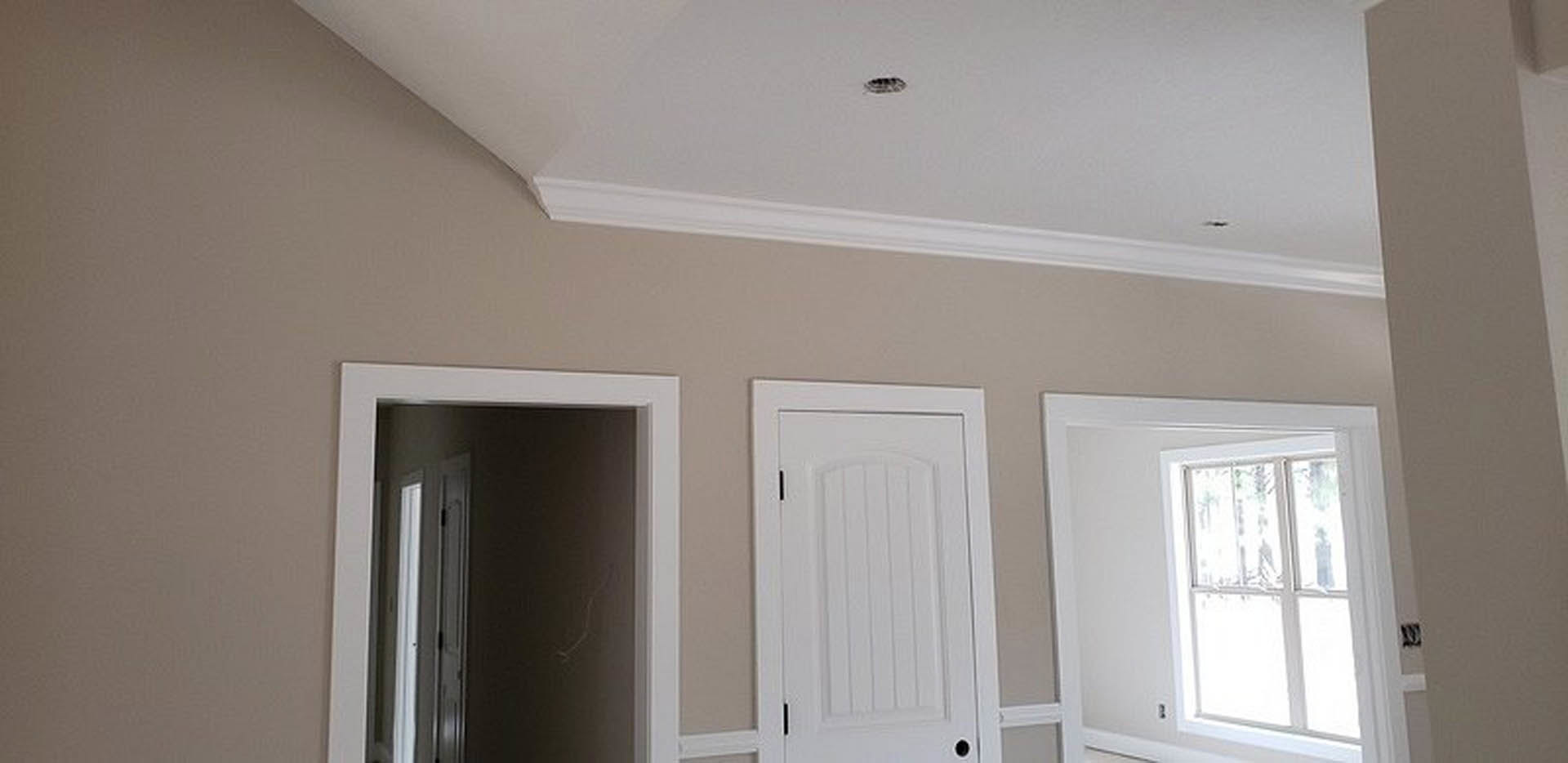 Hallway with white paneled doors, white door frames, light-colored walls, and a window with a white frame; open door reveals adjacent room, black and white object rests on white