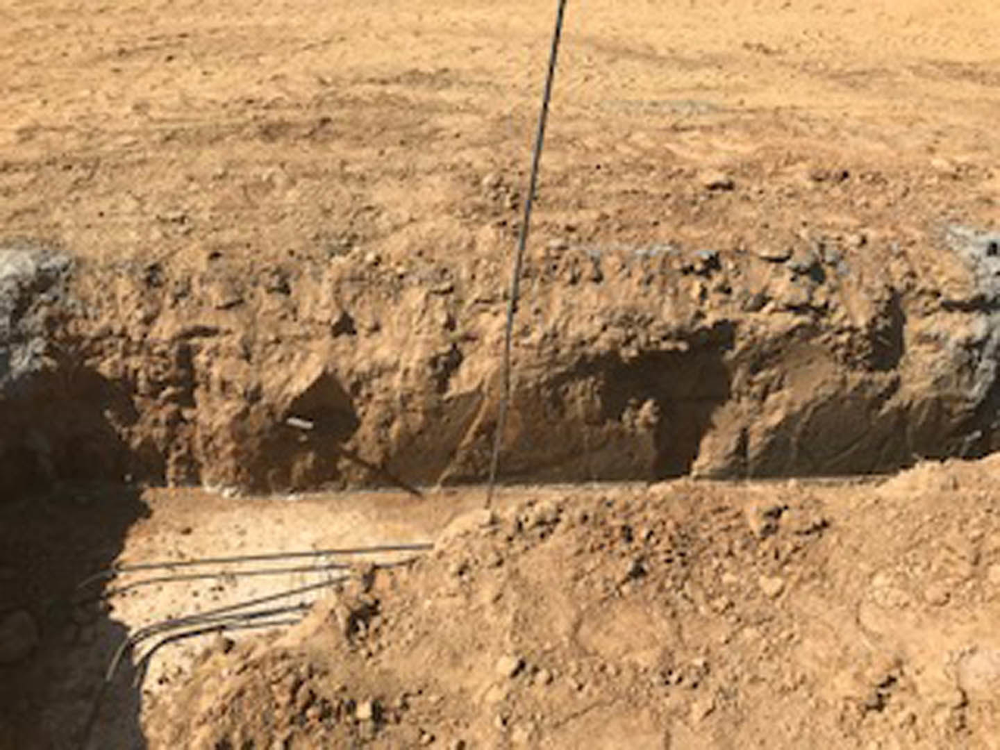 Excavated dirt hole outdoors with exposed electrical wires and scattered rocks
