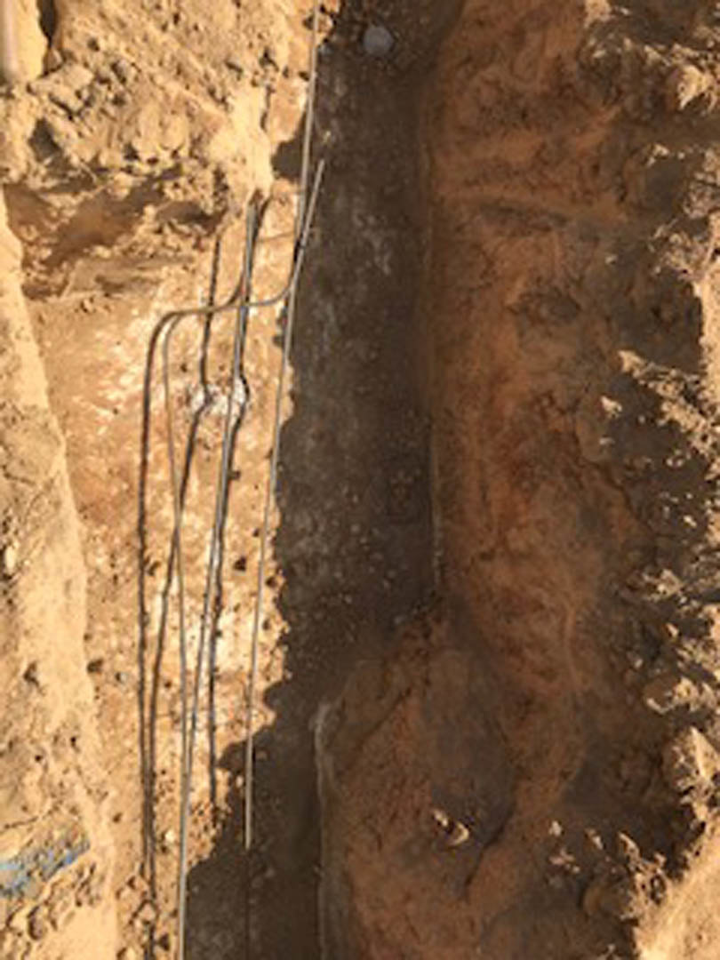 Exposed wire emerging from soil in a small hole on brown earth, surrounded by rocks and outdoor ground materials