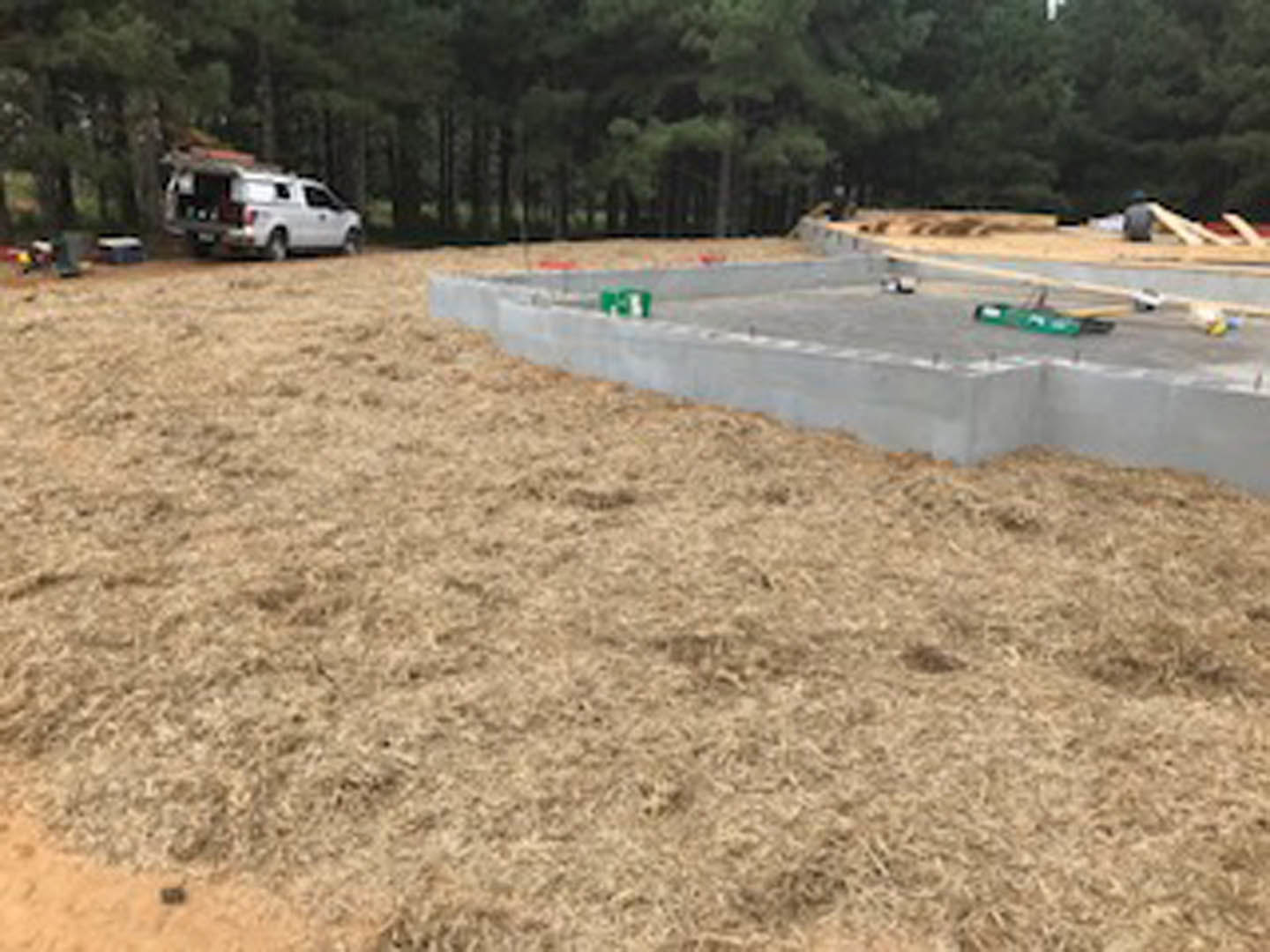 Concrete foundation surrounded by grassy field, white truck parked nearby, trees in background