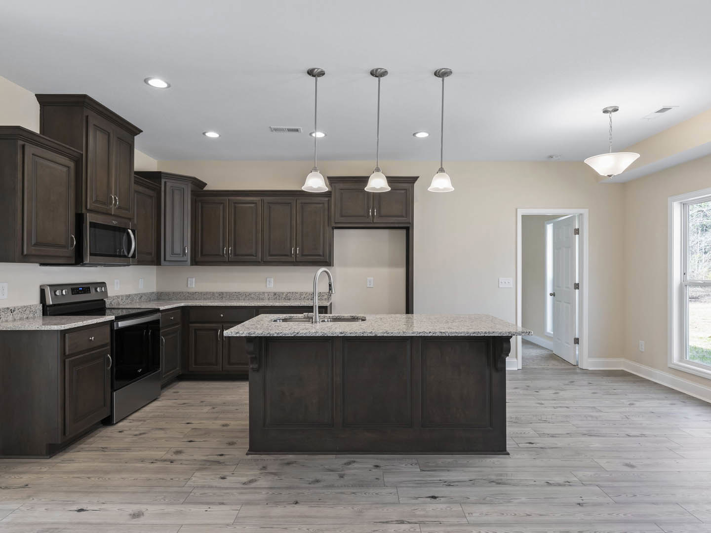 Modern kitchen featuring a central island with built-in sink, stainless steel stove, white cabinetry, tiled backsplash, stone countertops, recessed ceiling light, and a window with
