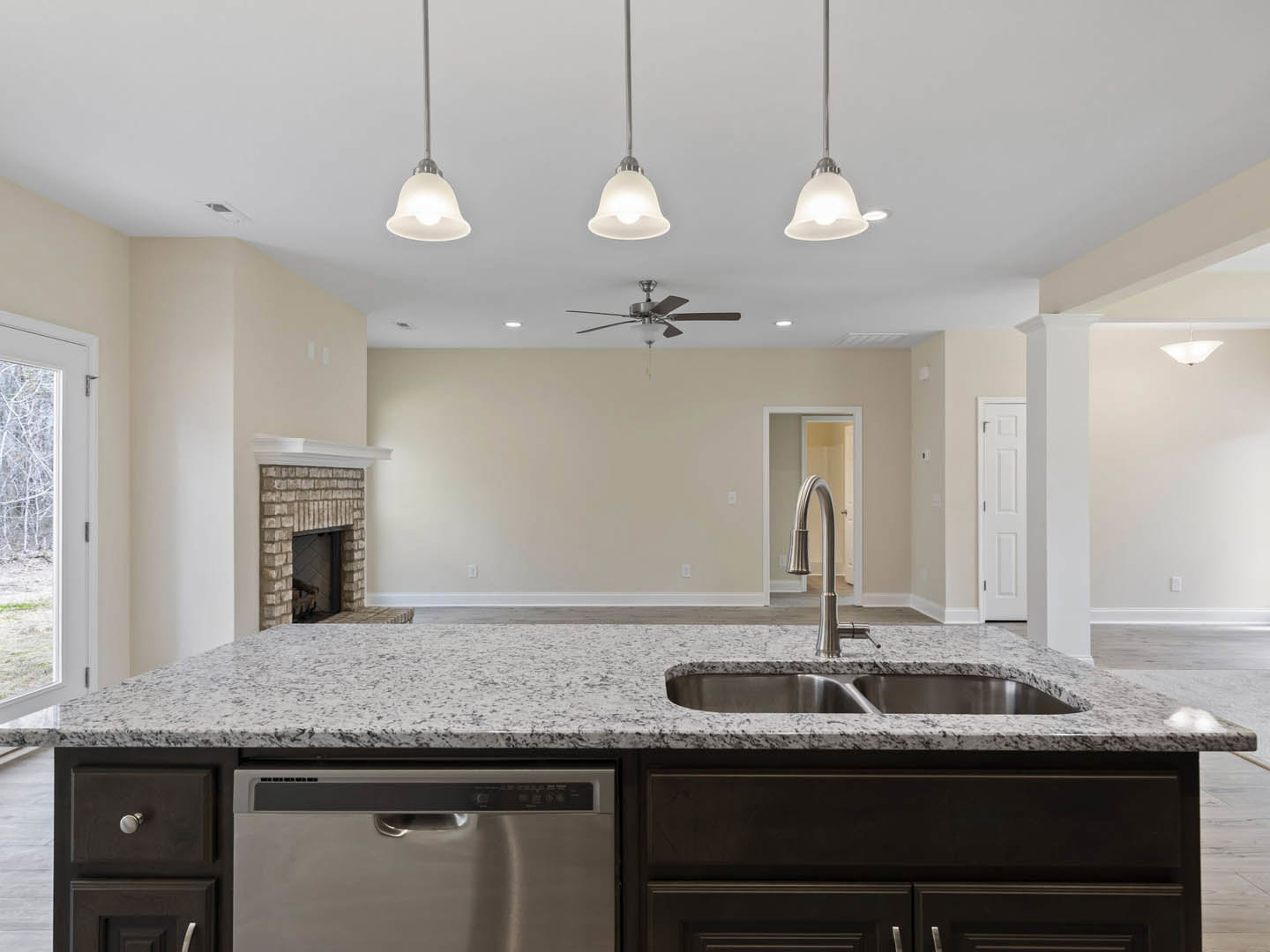 Quartz kitchen island with built-in sink and stove, white cabinetry, stainless steel dishwasher, tile backsplash, large window overlooking trees, metal ladle resting near sink