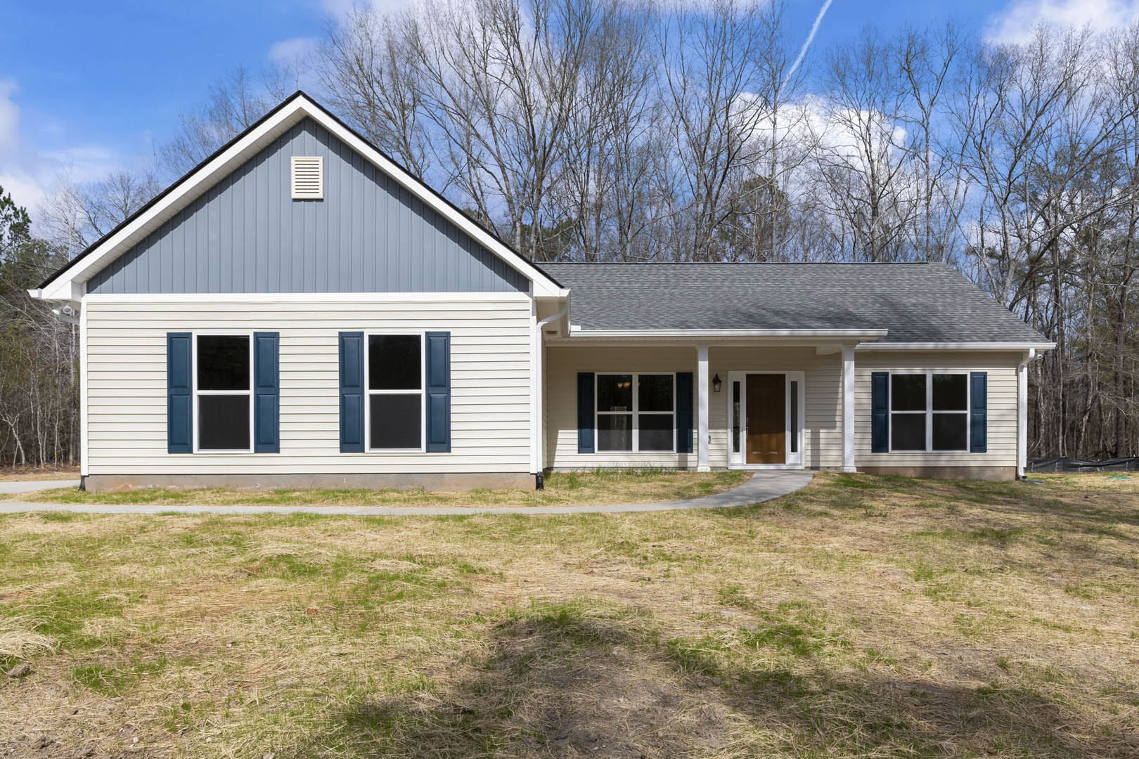 Two-story house with blue roof, white-framed windows, and white siding, surrounded by green lawn and mature trees under partly cloudy sky
