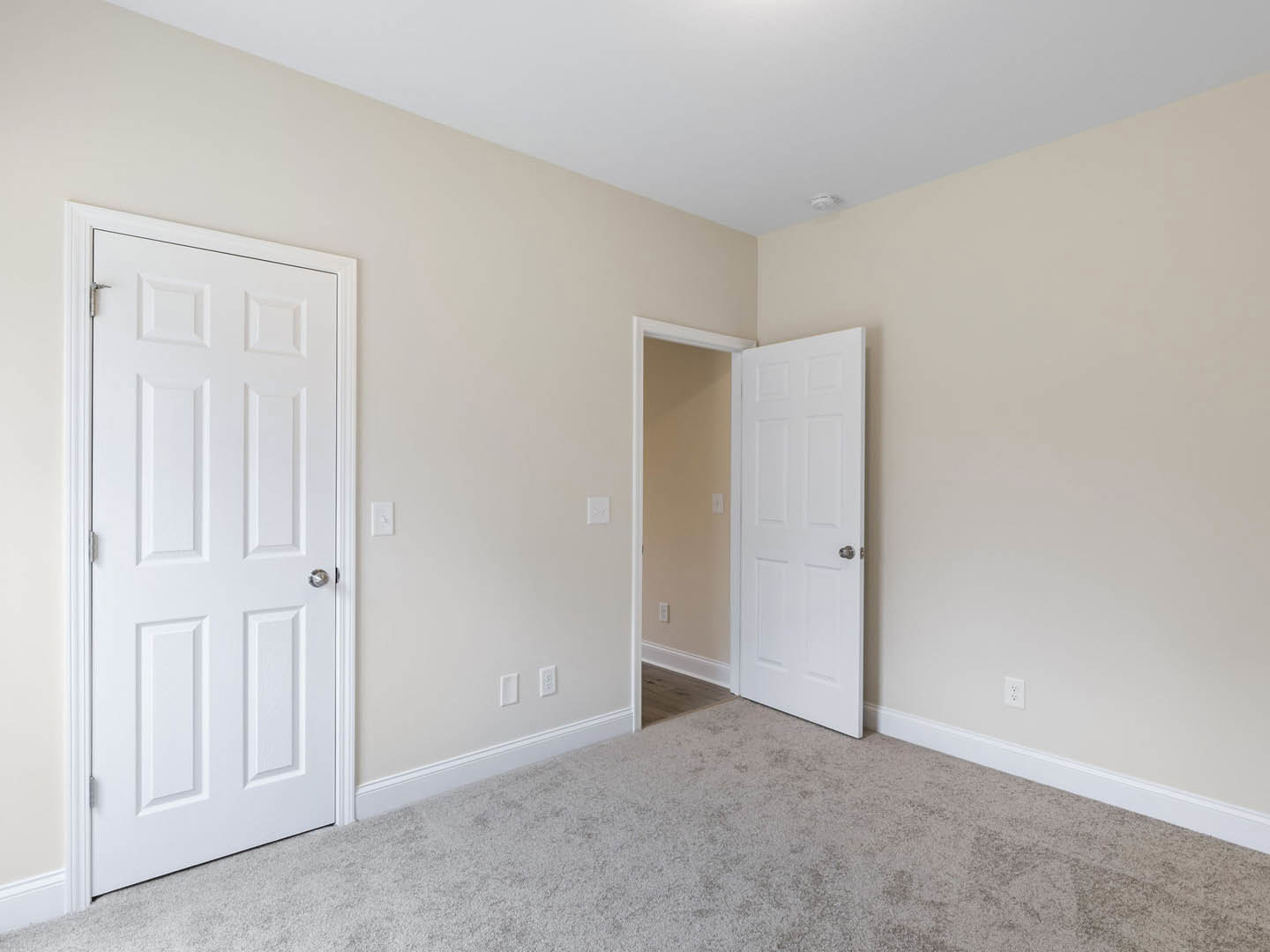 White paneled doors with silver knobs, light switch on wall, beige carpeted floor in a residential room