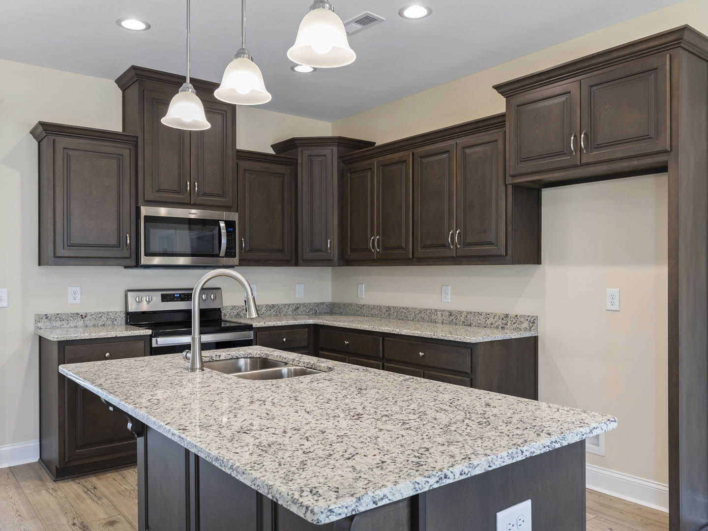 Kitchen with dark wood cabinets, marble countertop, stainless steel microwave, double sink, and bell-shaped pendant light fixture
