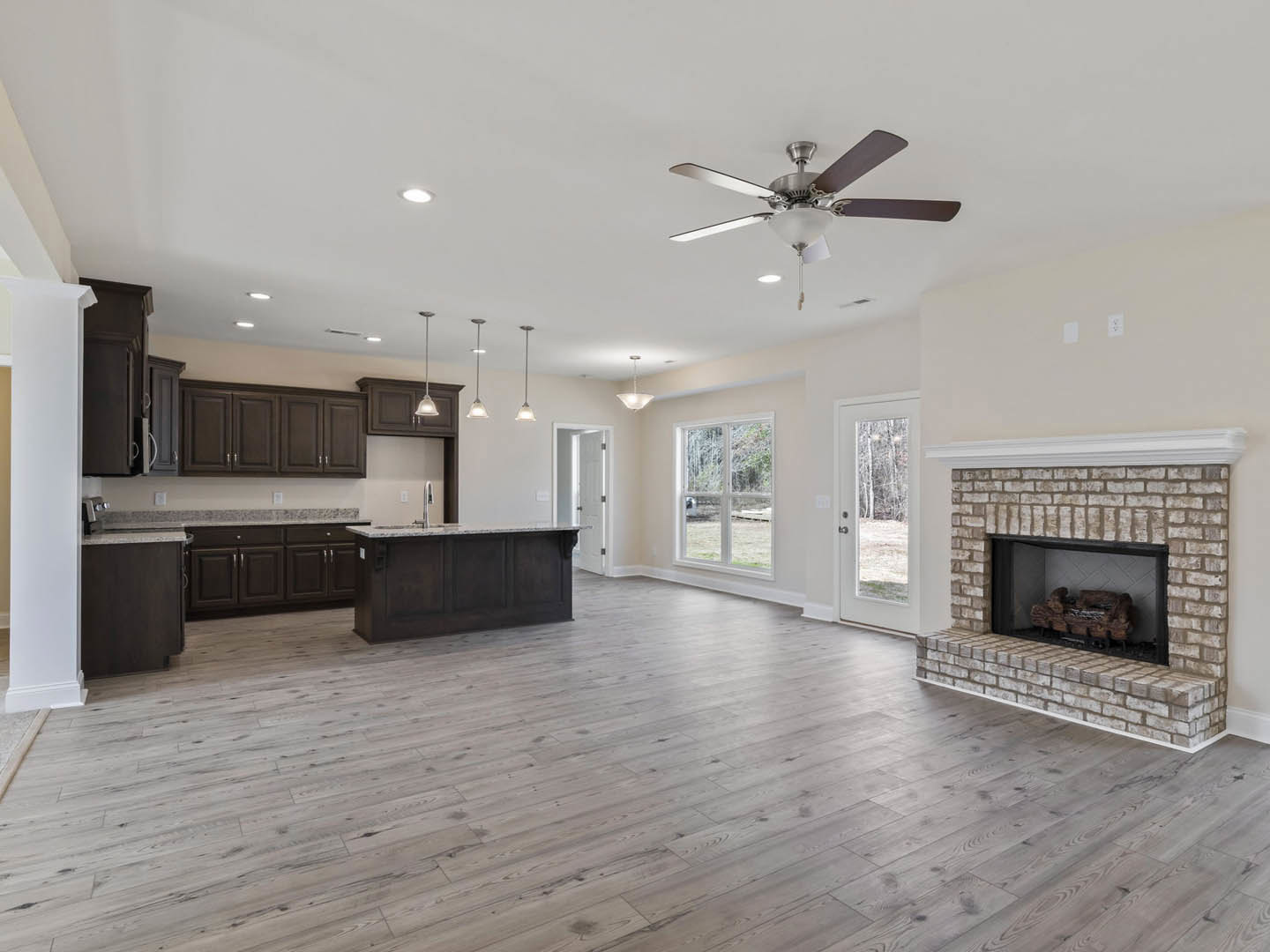 Spacious open-concept living area featuring hardwood floors, marble kitchen countertops, white cabinetry, a stone fireplace with a wood log, and a ceiling fan with light fixture