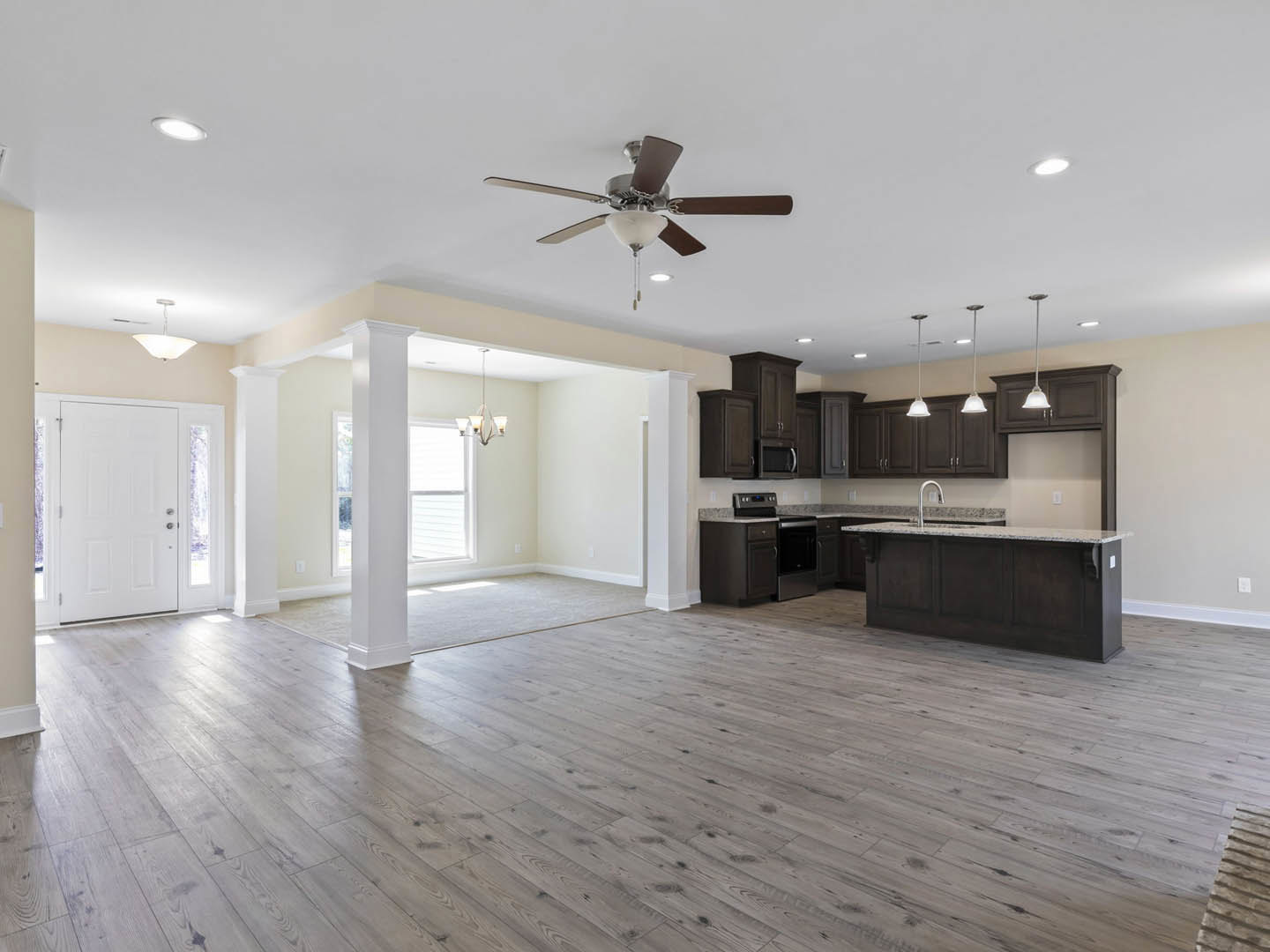 Spacious open floor plan featuring hardwood flooring, kitchen with cabinetry and countertops, adjacent dining area, ceiling fan with light fixture, white door with glass panels