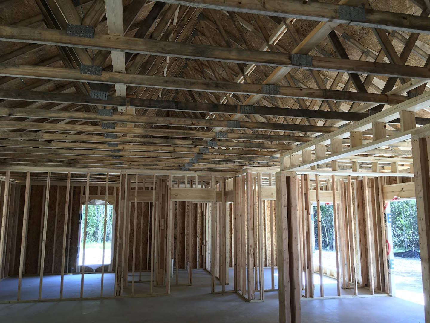 Exposed wooden ceiling beams over a concrete floor, unfinished walls, and large window overlooking forest