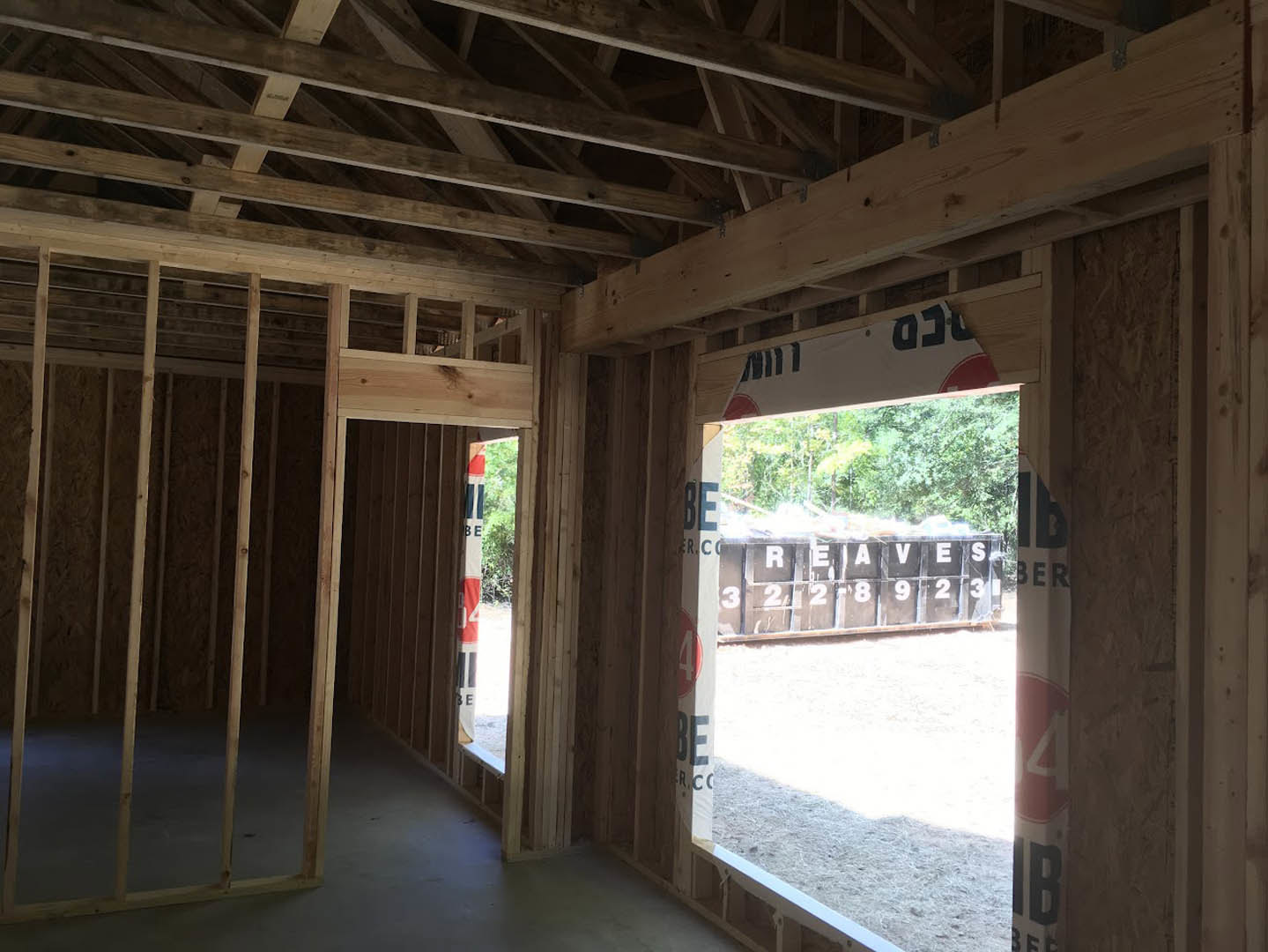 Wood-framed room featuring exposed beams, large window, and unfinished walls with visible lumber and planks