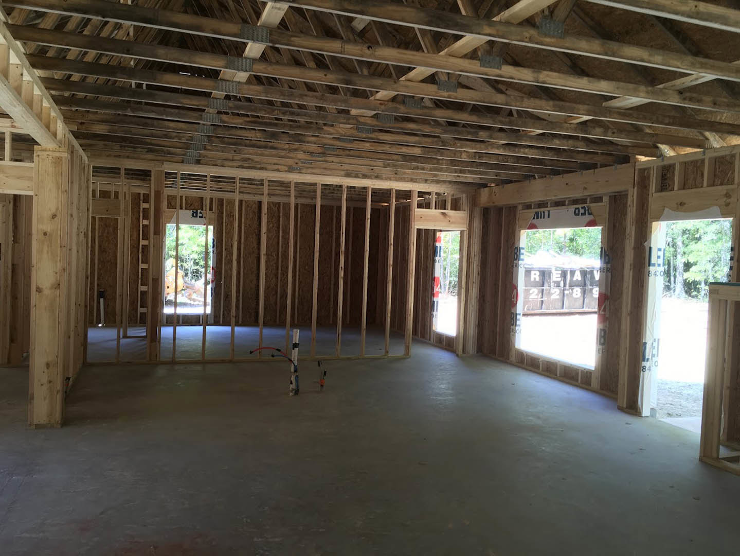 Wooden ceiling beams and plank roof above a concrete floor with exposed wiring, large window with a sign, unfinished interior walls