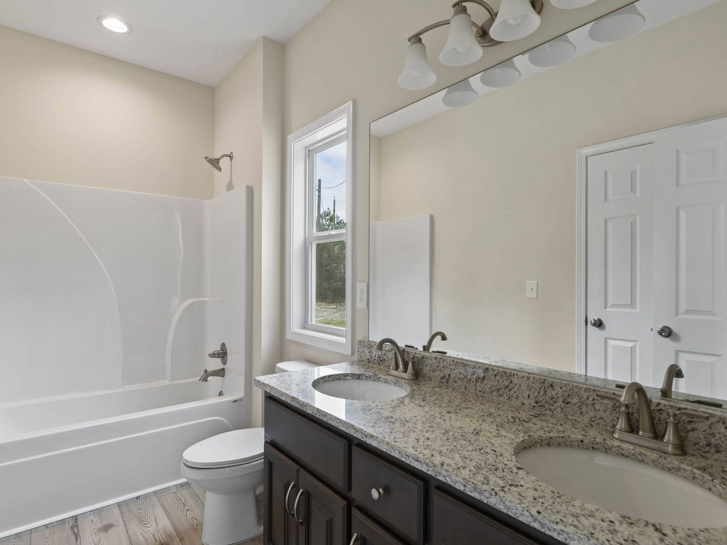 Bathroom with white tile walls, white toilet, pedestal sink, silver faucet, bathtub, and window showing outdoor telephone pole