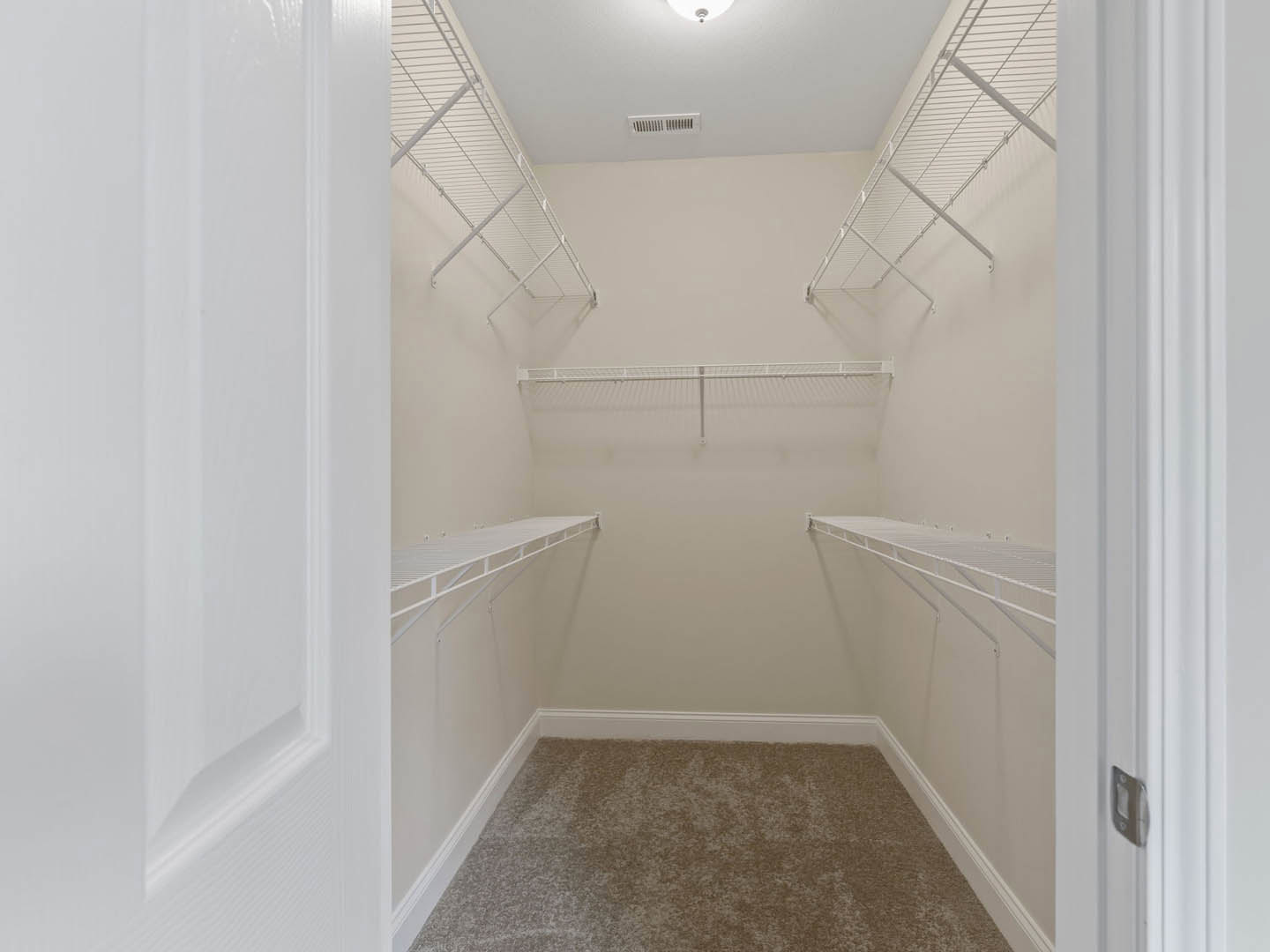 Walk-in closet with white shelving, carpeted floor, and a white door featuring a silver handle