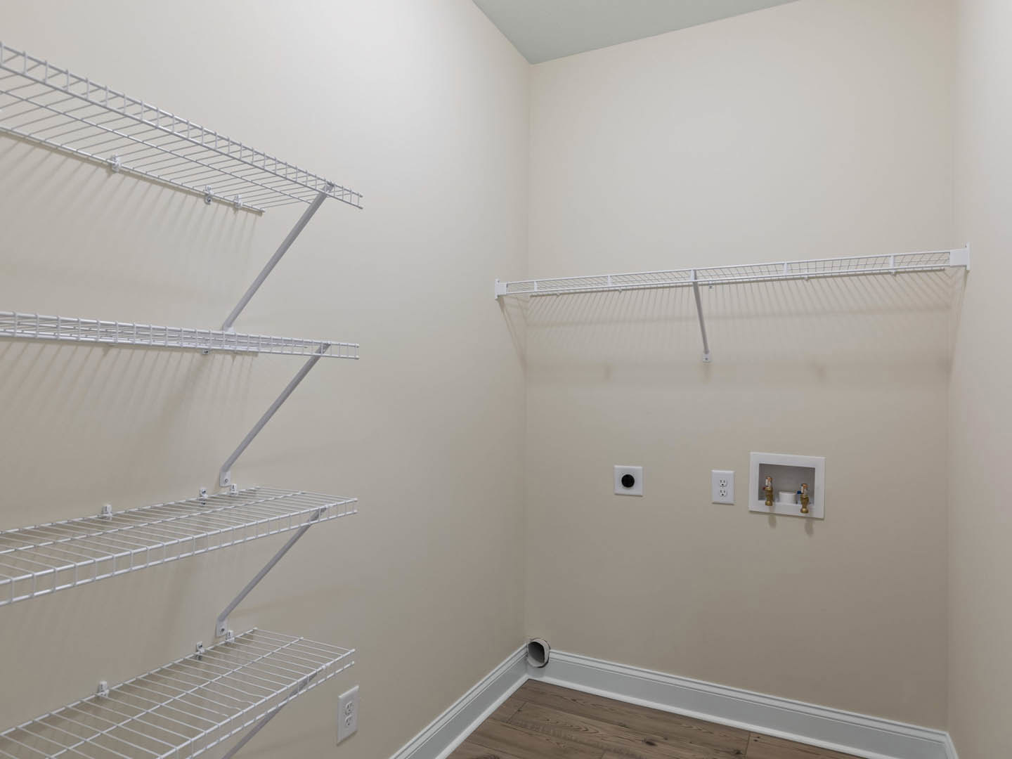 Wood floor room with white wire shelving mounted on plaster walls, two brass faucets above a rectangular utility sink, and electrical outlets visible near shelving.