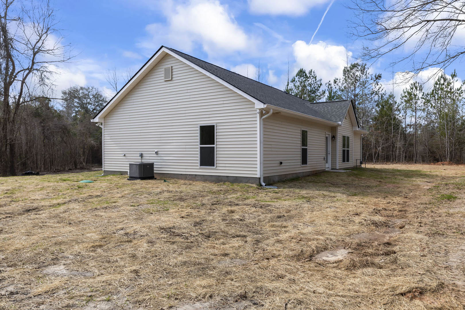 White siding house with large windows, black trim, grassy front yard, mature trees, and cloudy sky in the background
