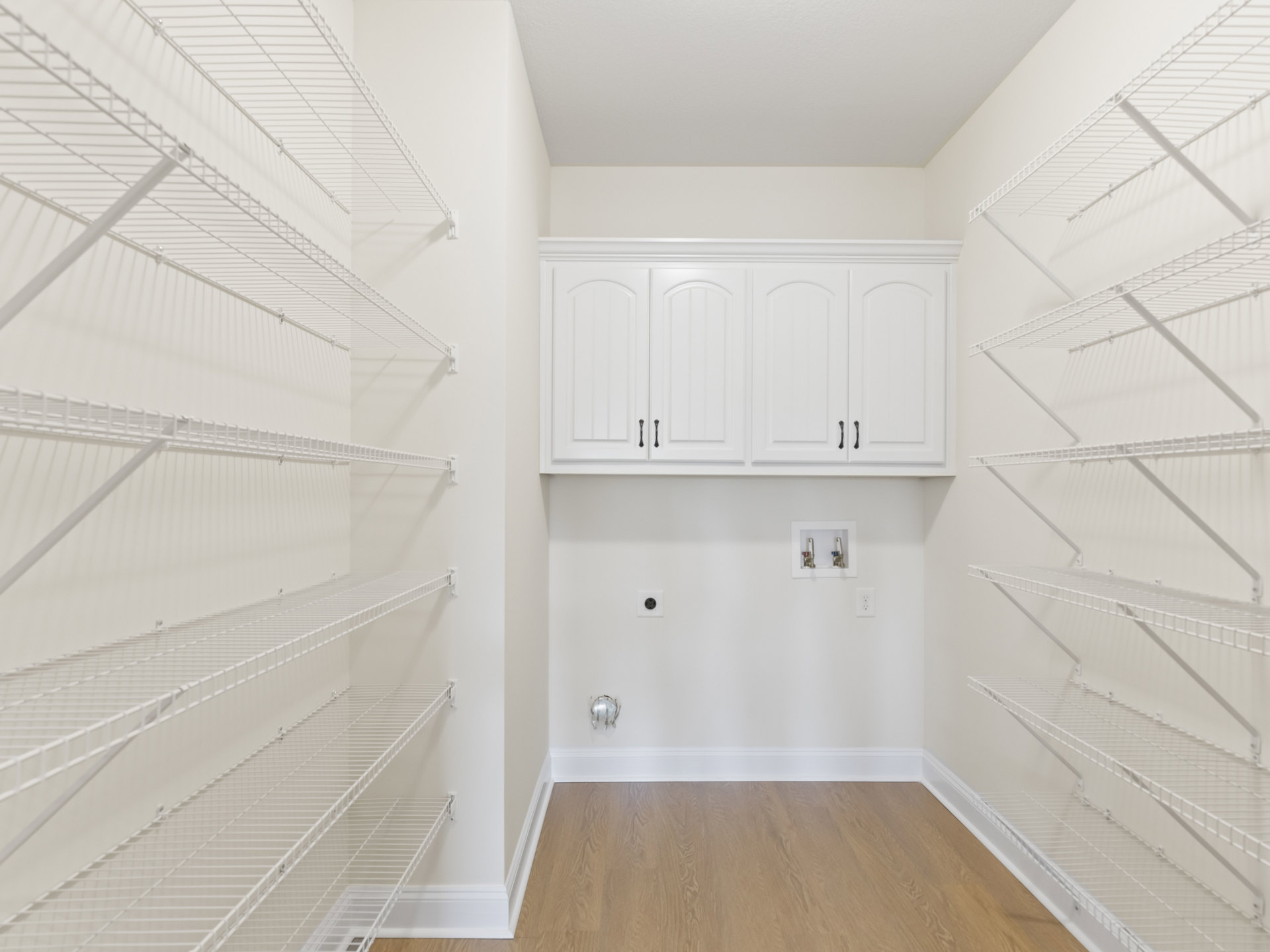 White built-in shelves and cabinets with black handles, metal rods on shelving, white walls and ceiling, light flooring, simple molding.