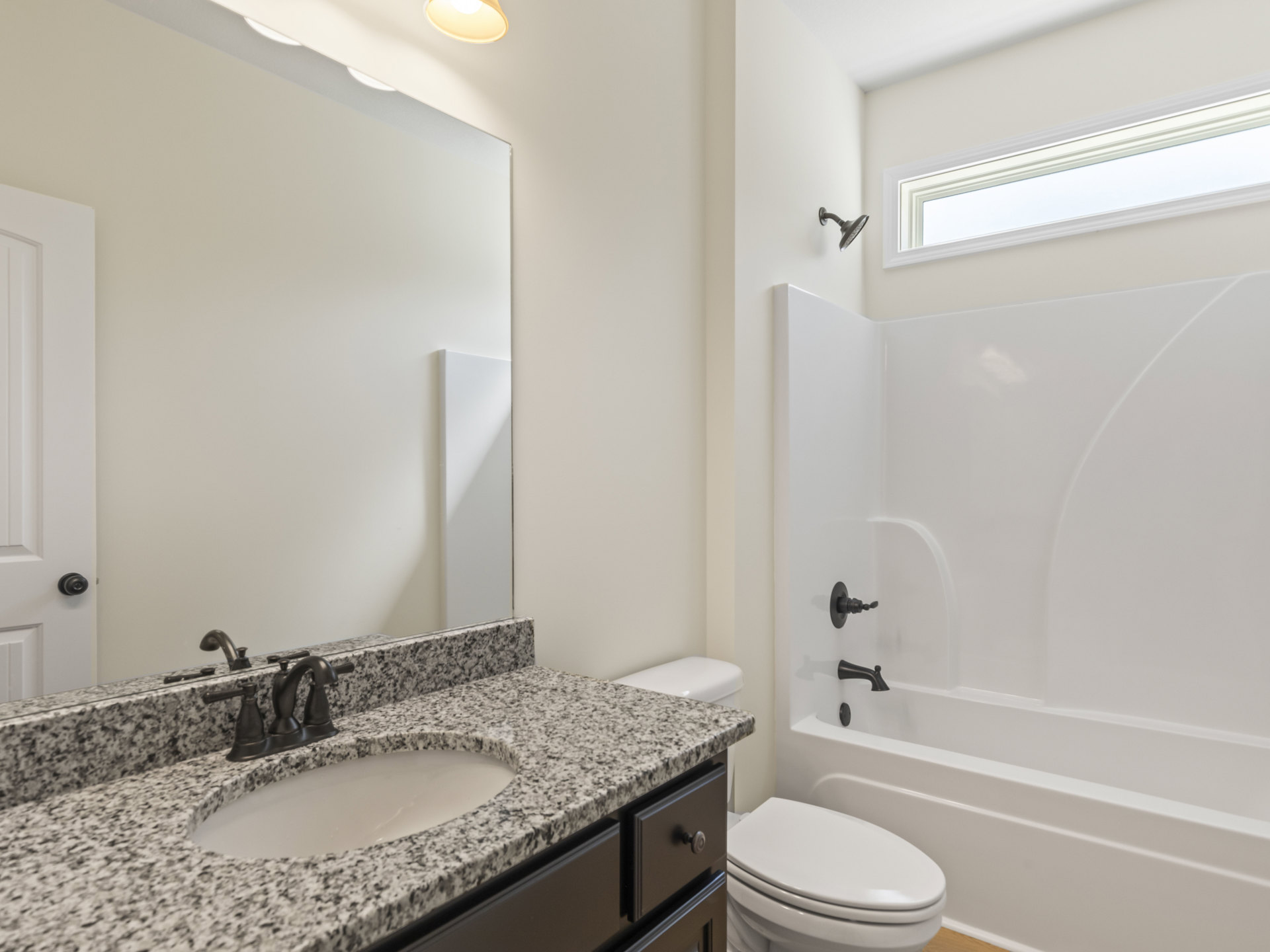 Modern bathroom featuring a white sink with black faucet, closed toilet seat, freestanding white bathtub with chrome fixtures, light-colored tile walls, and a window allowing