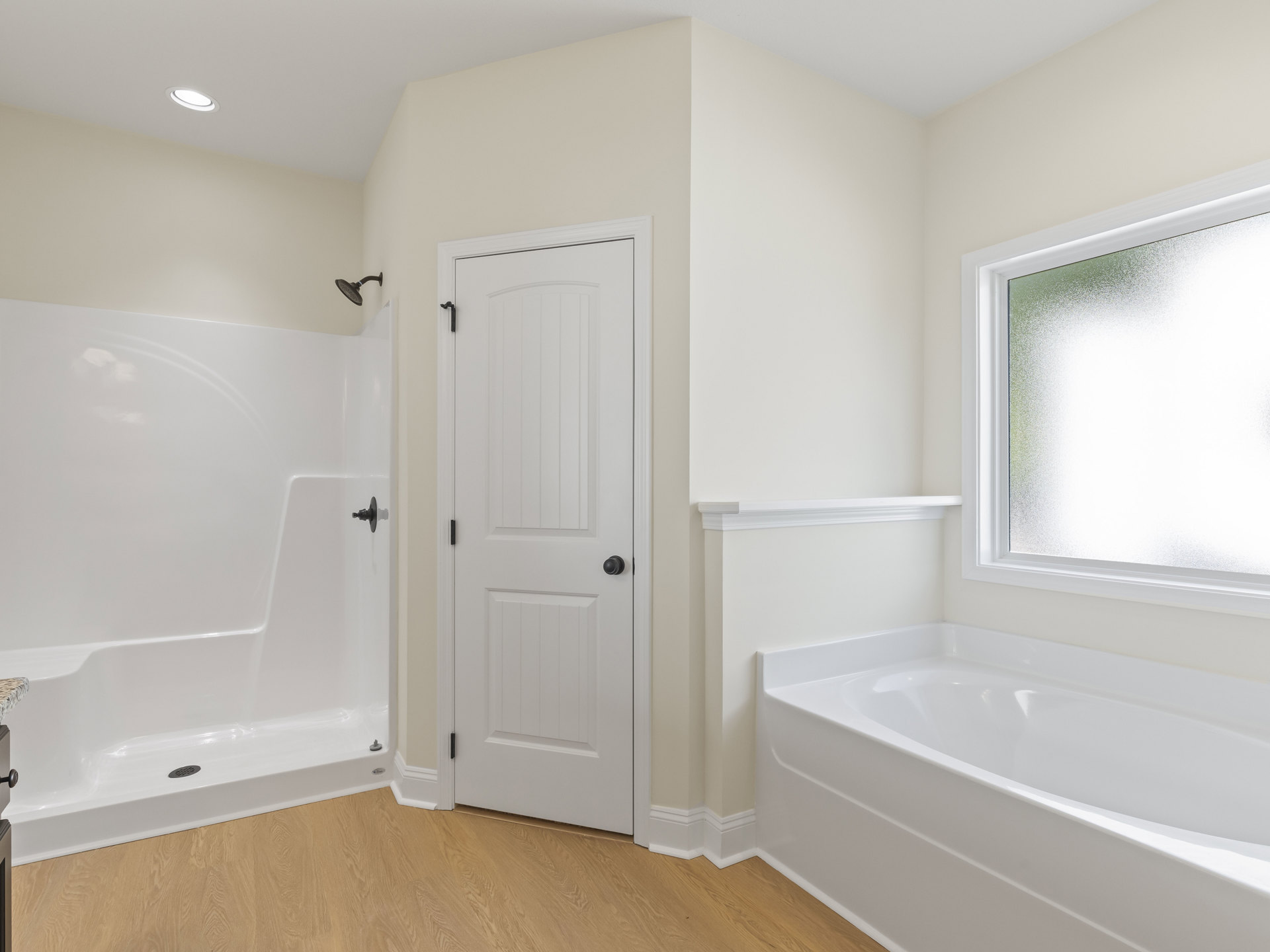 Bathroom with white freestanding bathtub, frosted glass window, white door with black knob, black shower head, light tile floor and walls