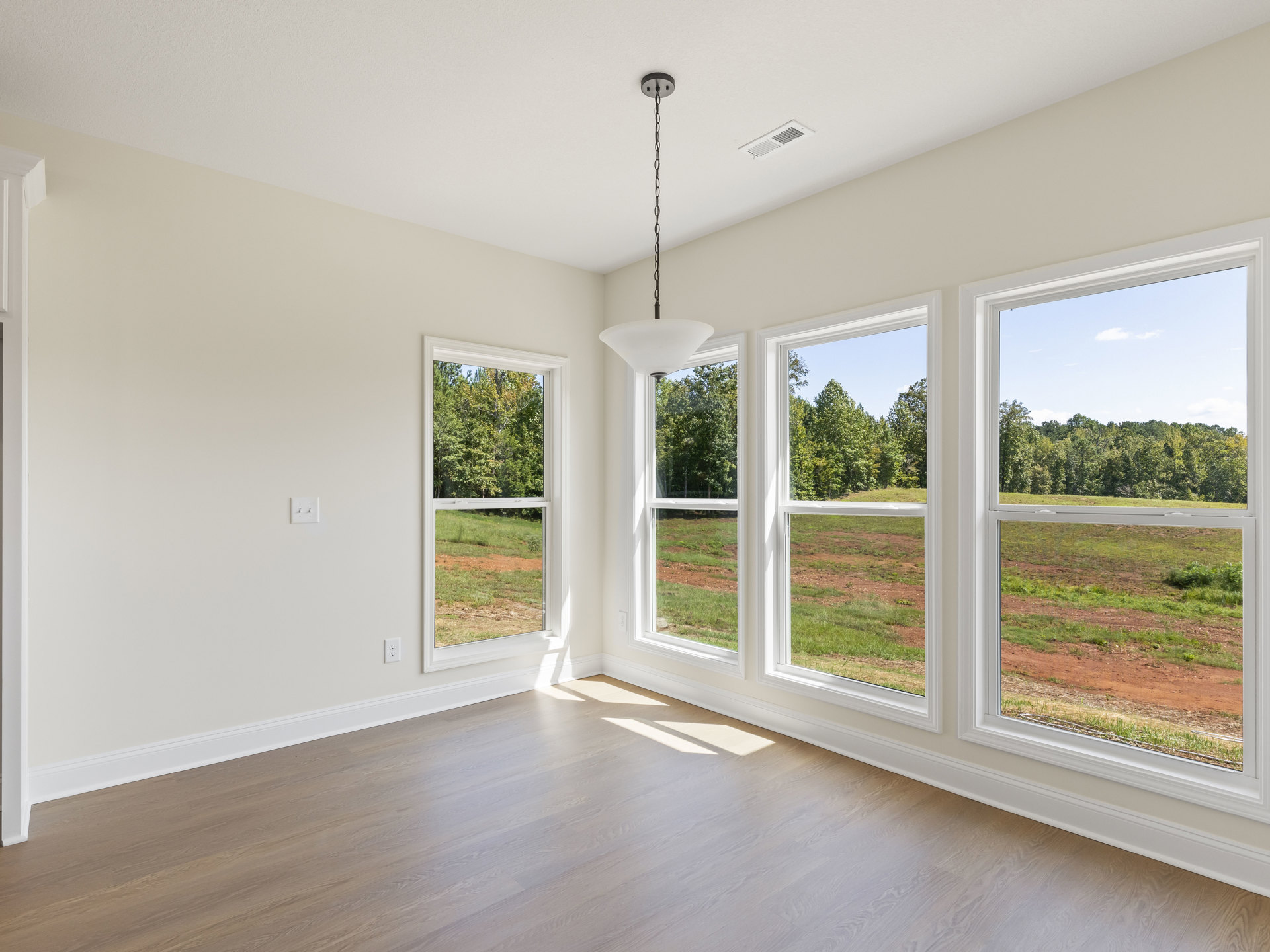 White-walled room with large windows, wood laminate flooring, ceiling vent, and view of grassy field outside